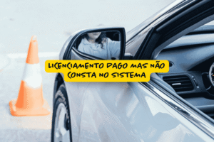 Carro prateado parado ao lado de um cone de sinalização laranja, com motorista refletido no retrovisor e faixa amarela com a frase "Licenciamento pago mas não consta no sistema", destacando um problema comum no processo de licenciamento veicular.
