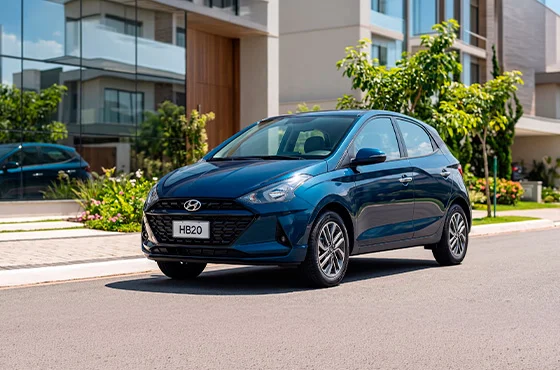 Hyundai HB20 2026 azul estacionado em frente a um condomínio residencial moderno, destacando o design compacto e contemporâneo do hatch. A imagem ilustra uma opção de carro para mulher, unindo conforto, tecnologia e praticidade para o uso diário.