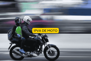 Dois motociclistas com capacetes circulam em via urbana sobre uma moto preta, em movimento rápido. No centro da imagem aparece um selo amarelo com a inscrição “IPVA de moto”, relacionando a cena ao imposto veicular obrigatório.