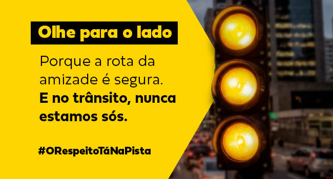 Semáforo amarelo aceso em avenida urbana movimentada com mensagem educativa sobre segurança no trânsito e respeito entre motoristas, destacando a campanha “Olhe para o lado” e a importância da amizade no trânsito seguro (banner mobile)