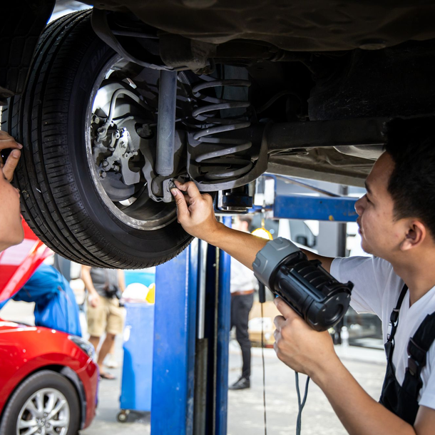 Mecânicos inspecionam mola e amortecedor da suspensão de um carro elevado na oficina.