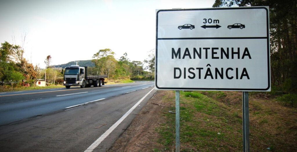 Placa educativa orienta motoristas a manter distância para evitar colisão traseira.