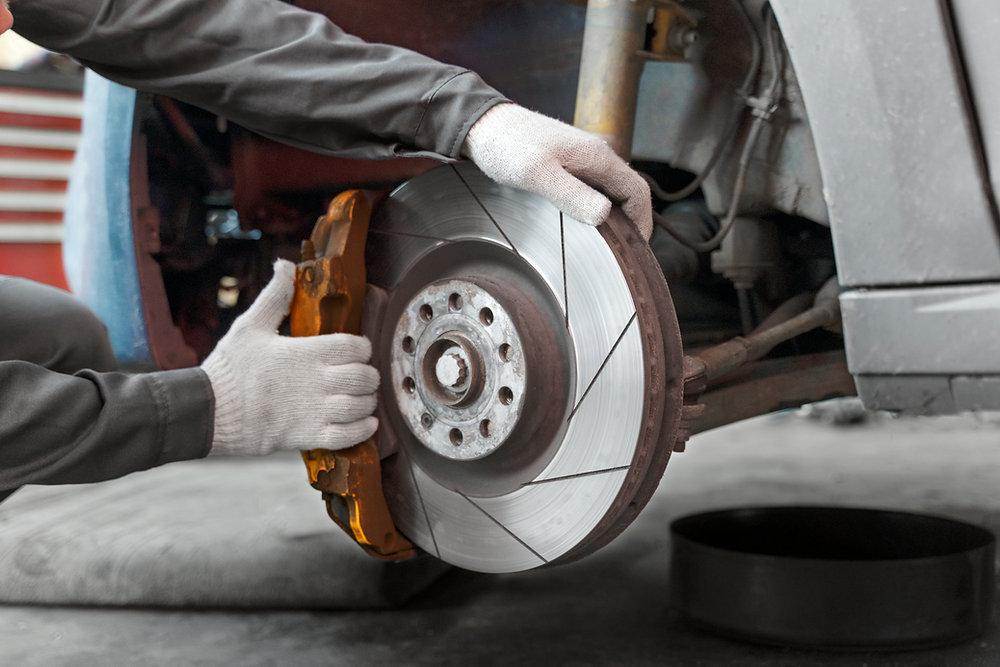 Mecânico inspeciona o disco e a pinça do sistema de freios de um carro durante manutenção em oficina.