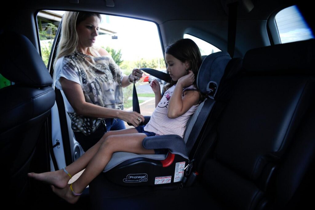 Responsável ajusta o cinto de uma criança no assento de elevação no banco traseiro do carro.