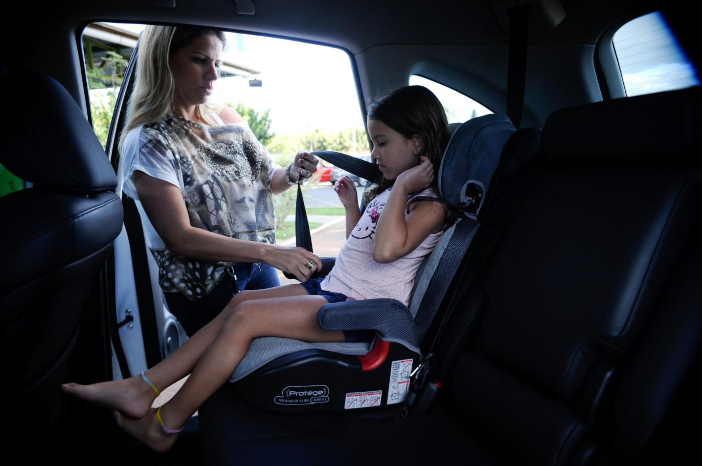 Responsável ajusta o cinto de uma criança no assento de elevação no banco traseiro do carro.
