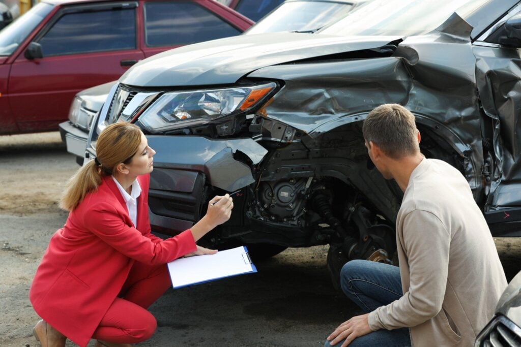 Vistoriadora avalia os danos na parte dianteira de um carro após acidente para análise da seguradora.