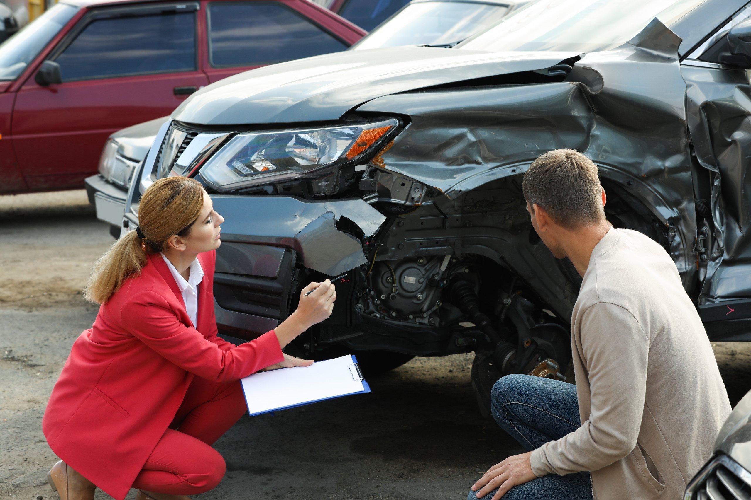 Vistoriadora avalia os danos na parte dianteira de um carro após acidente para análise da seguradora.